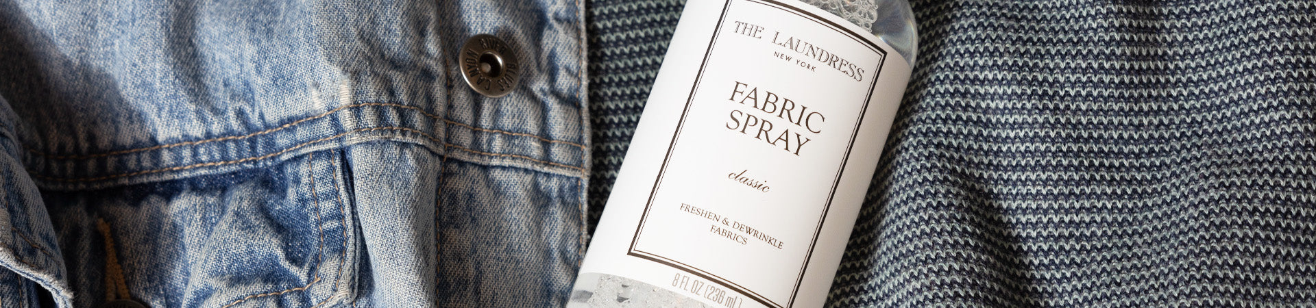 The Laundress Fabric Spray in the scent Classic for freshening and dewrinkling fabrics lays on a denim garment.