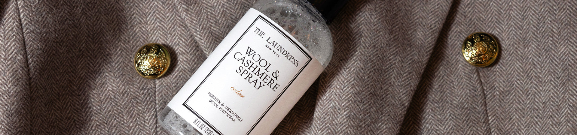 The Laundress Wool & Cashmere Spray in the scent Cedar, made to freshen & dewrinkle wool knitwear, lays on a wool jacket.