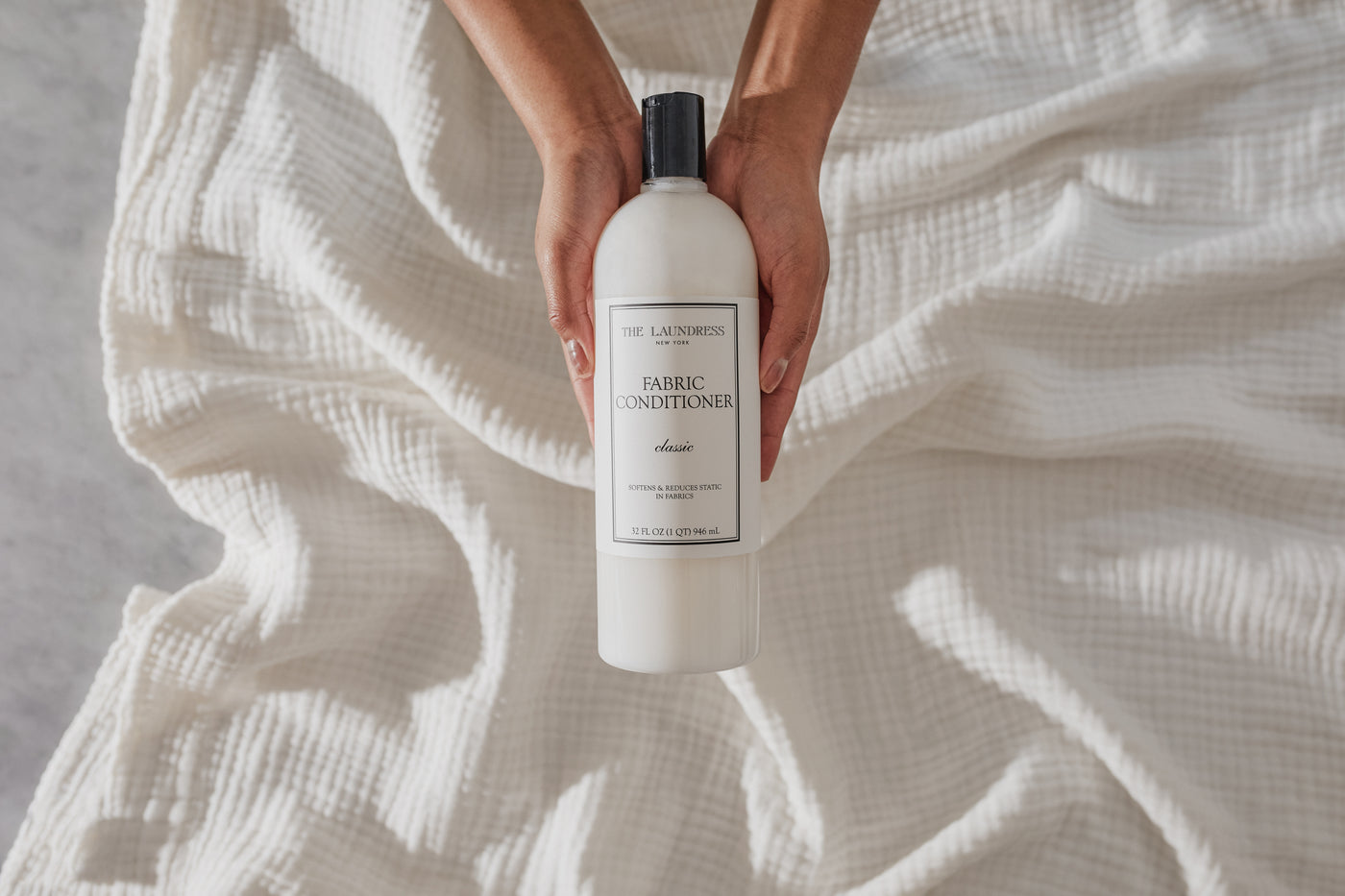 The Laundress Fabric Conditioner for softening and reducing static in fabrics held over white fabric.