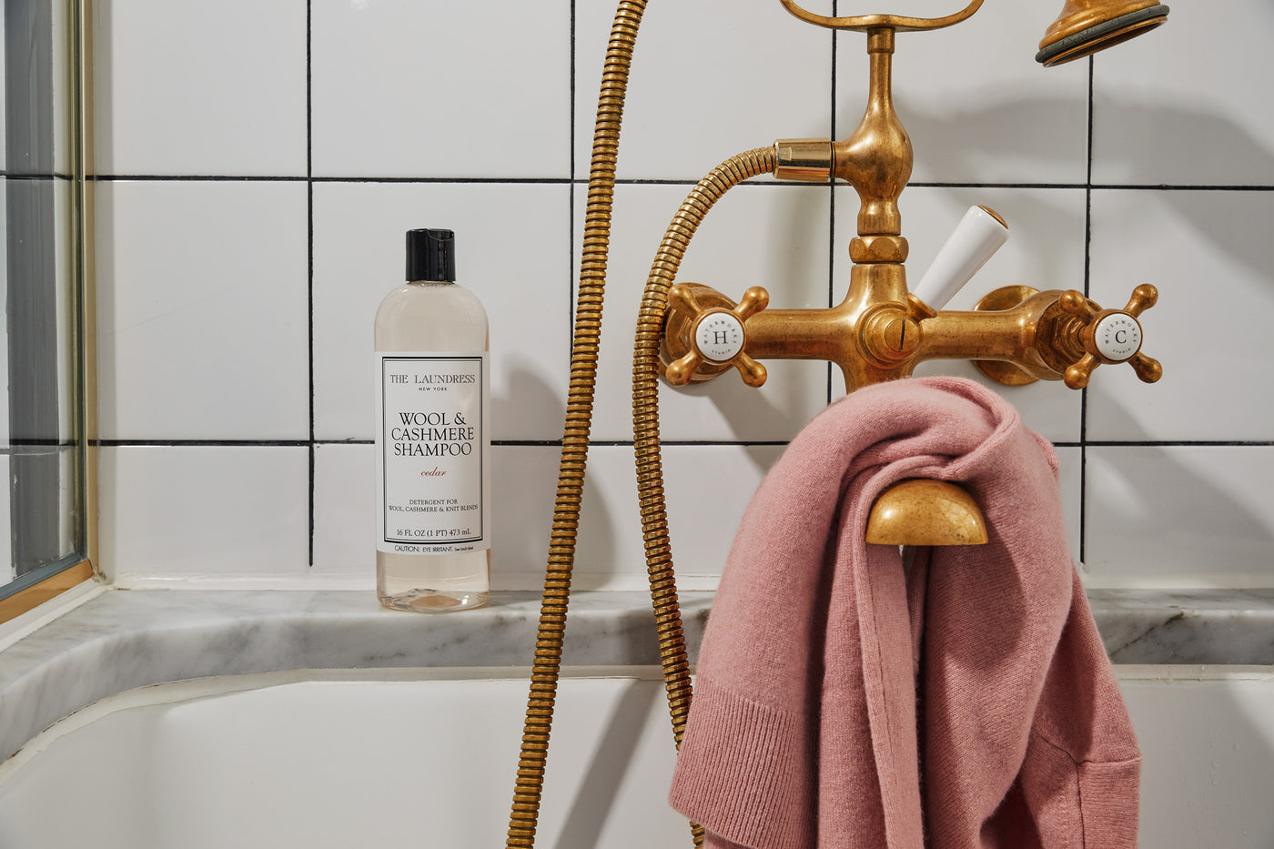 A bottle of The Laundress Wool & Cashmere Shampoo in the scent Cedar balancing on a ledge.