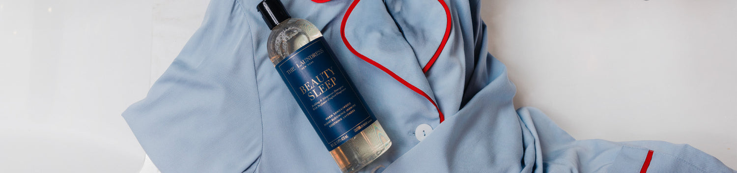 The Laundress Beauty Sleep Bedding & Sleepwear Detergent lays on top of a blue pajama set with a white background.