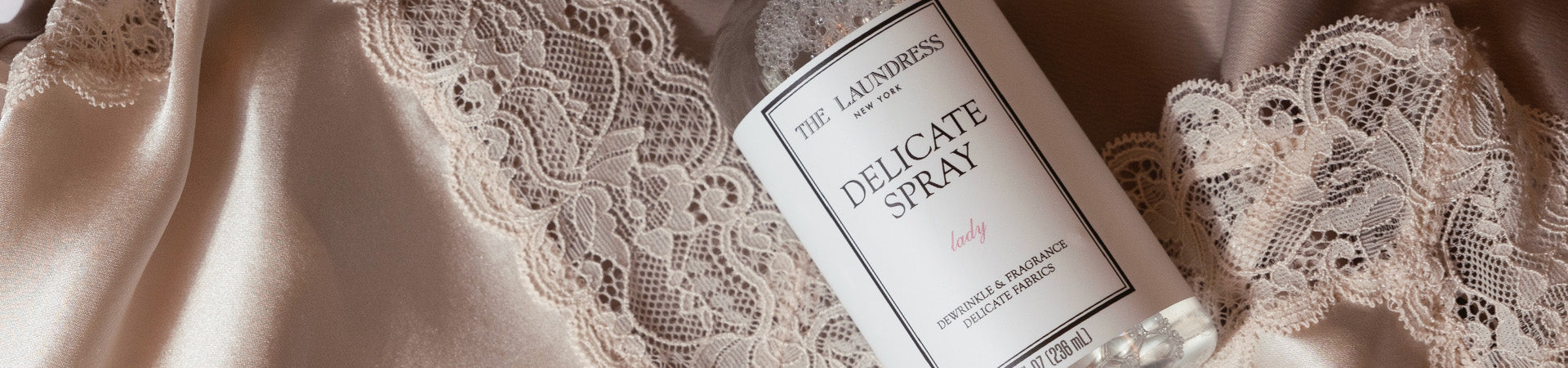 The Laundress Delicate Spray in the scent Lady, designed to dewrinkle and refresh silks, synthetics, and other delicates, sits on a pink silk and lace garment.