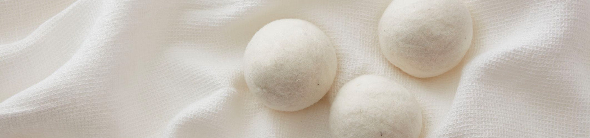 The Laundress Dryer Balls rest on a soft, creamy fabric with gentle folds, suggesting a sense of comfort and relaxation.