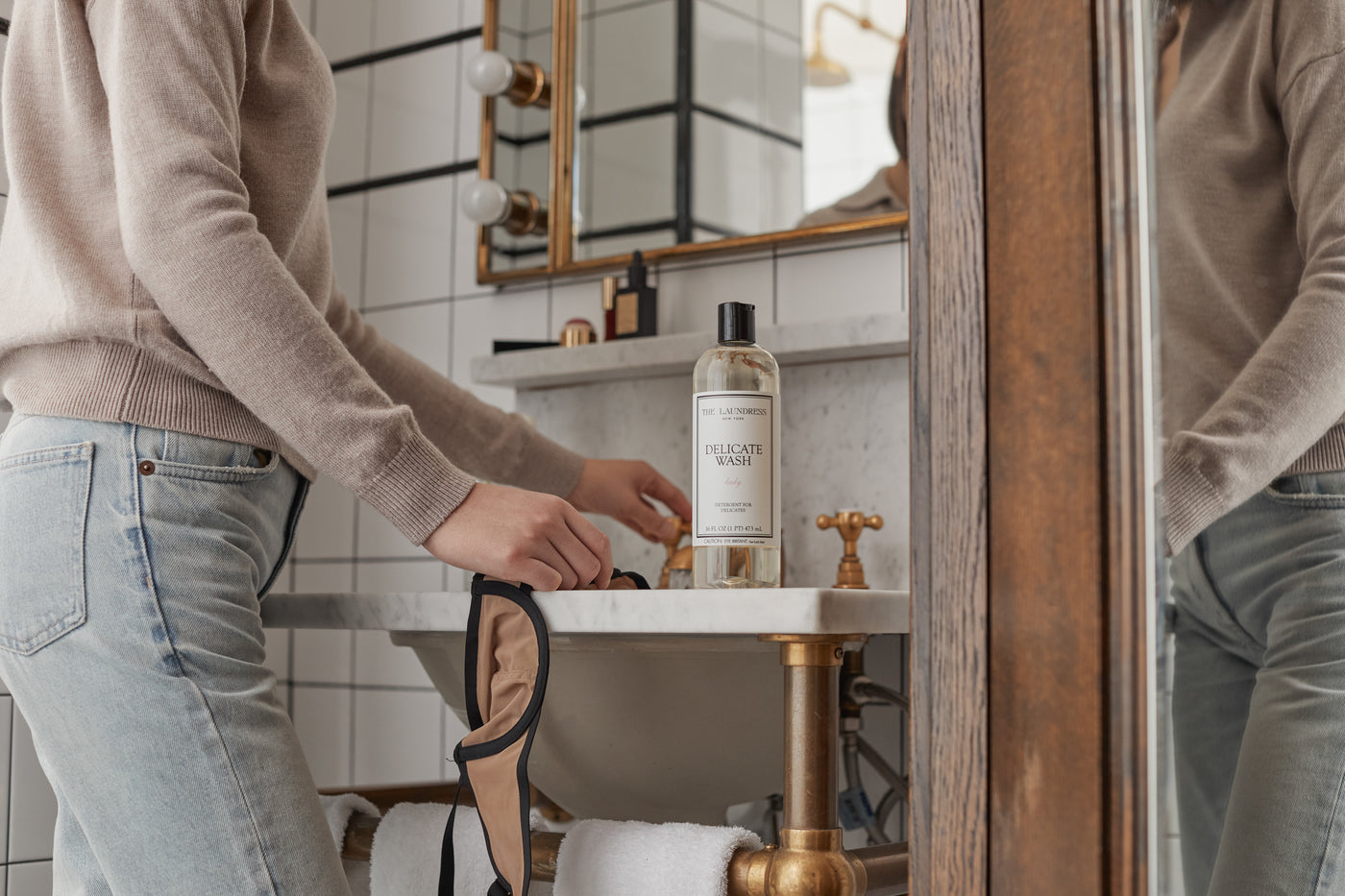 The Laundress Delicate Wash bio-based delicates detergent sits on a sink ledge.