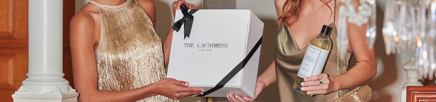 The Laundress Specialty Fabric Care Gift Set and The Laundress Signature Detergent being held up by two women dressed in gold.
