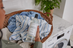 The Laundress Signature Detergent for everyday laundry and a basket full of clothes.